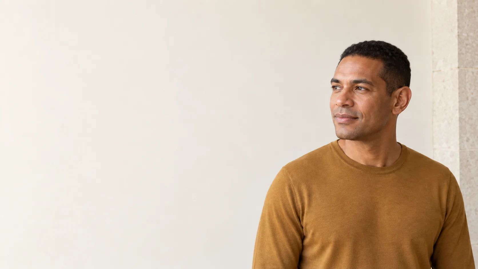 A fictional adult man in an ochre shirt stands beside an open ivory wall, with one ear naturally visible.