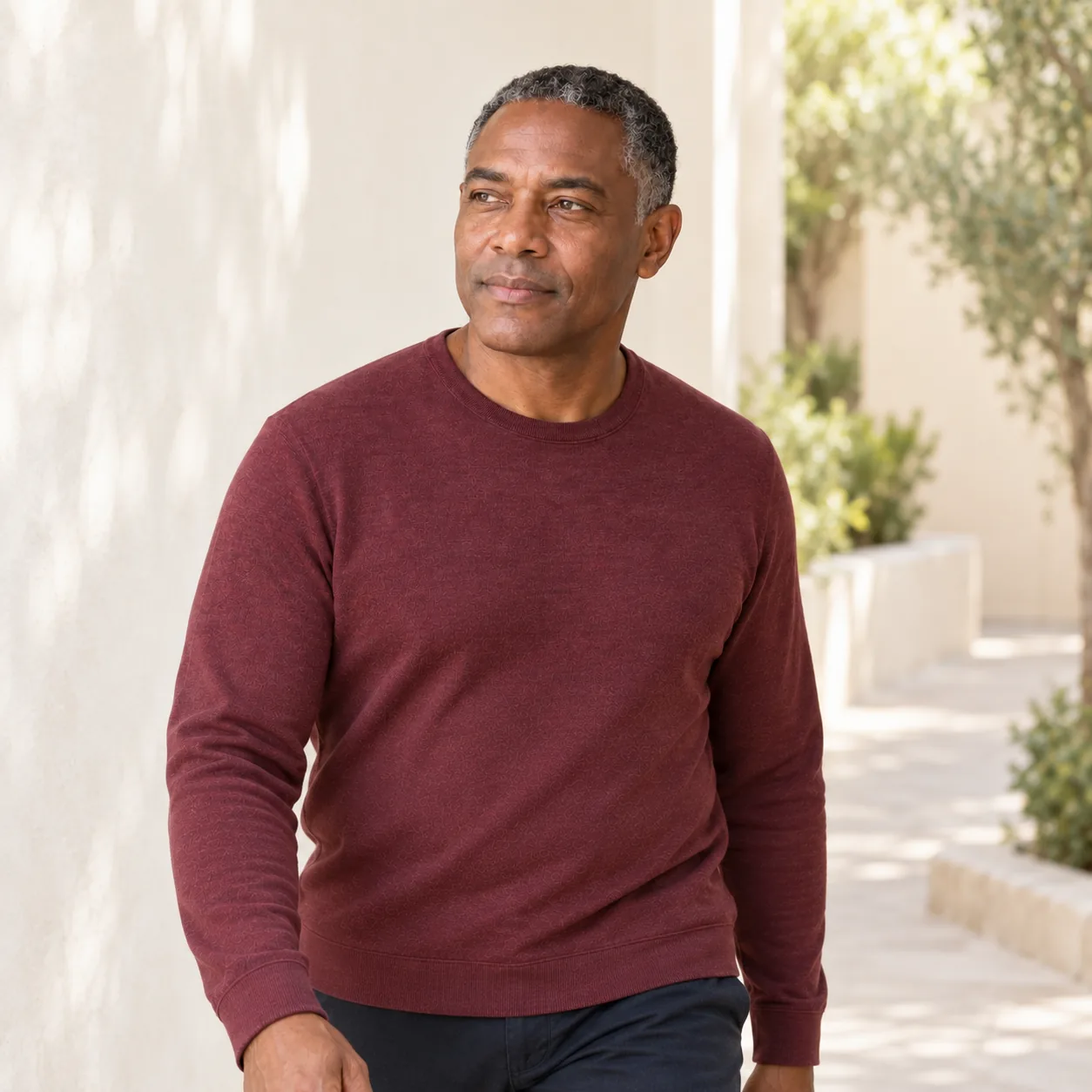 The same fictional adult man in a burgundy shirt walks calmly through an ivory courtyard with muted greenery.