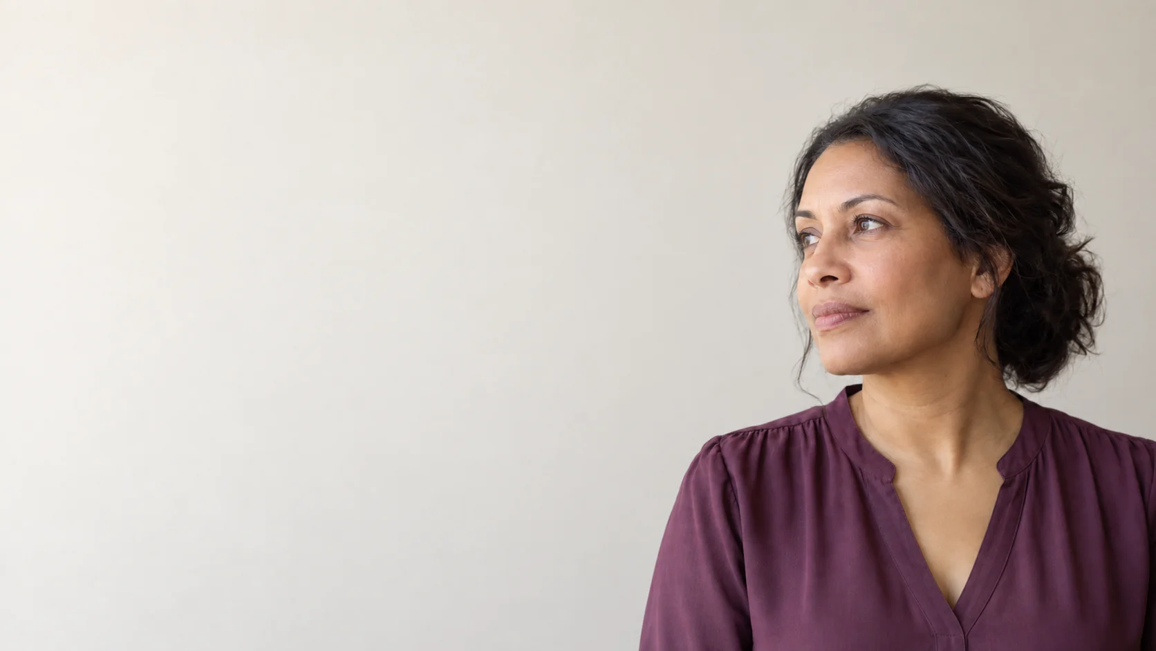 Editorial portrait of a fictional adult with a natural jaw and neck visible against a pale wall.