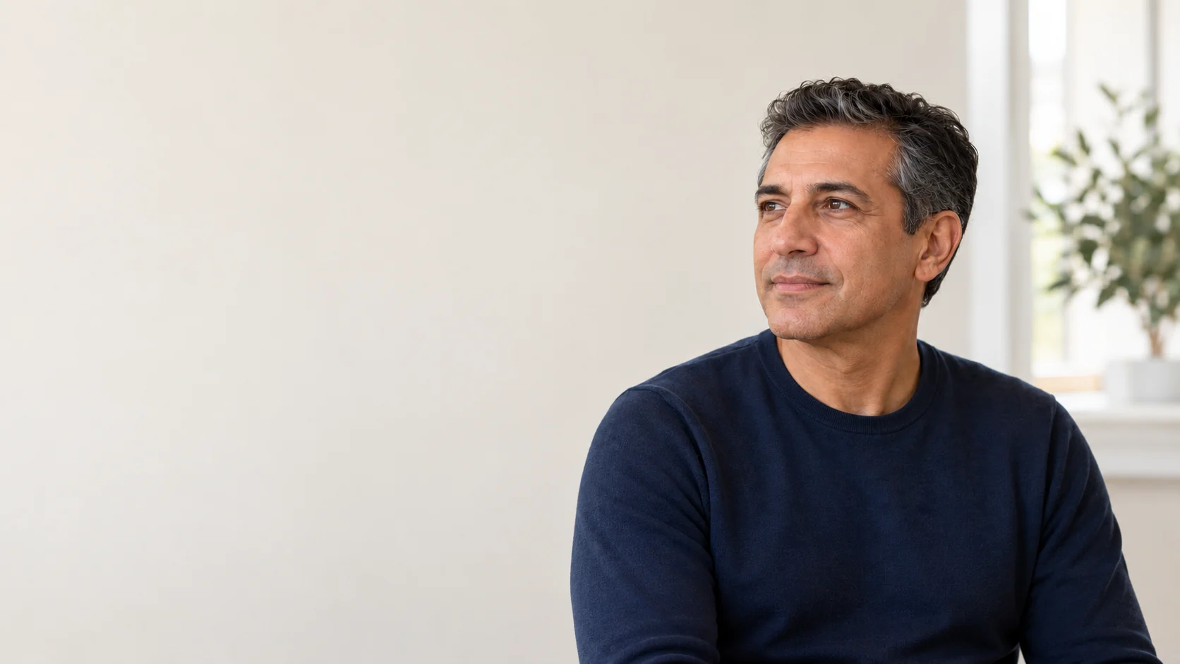 A fictional adult seated in a quiet room, with natural lower-face contour, visible ear, jawline and upper neck.