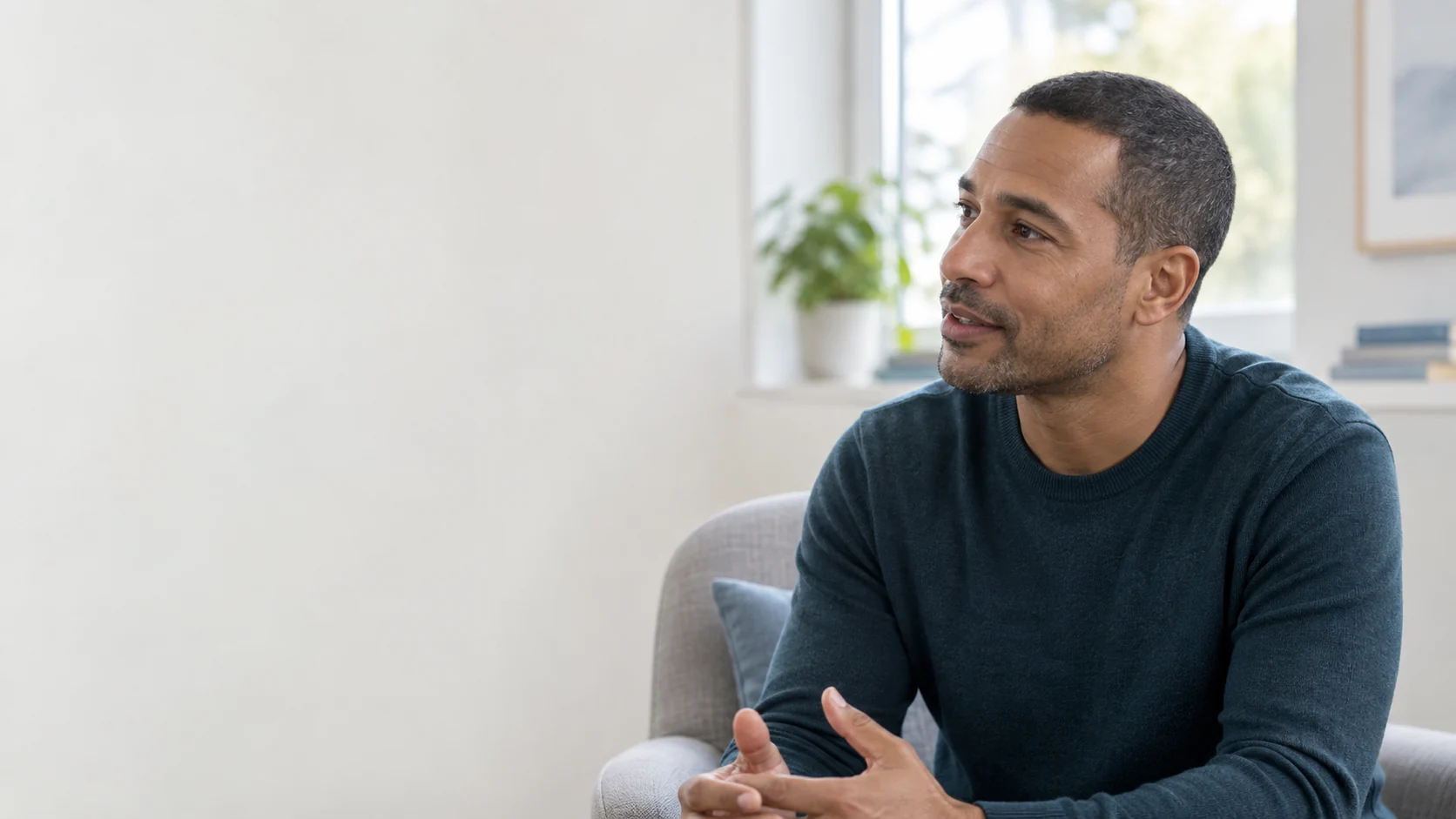 A fictional adult man in a dark blue sweater speaks in a softly lit room.