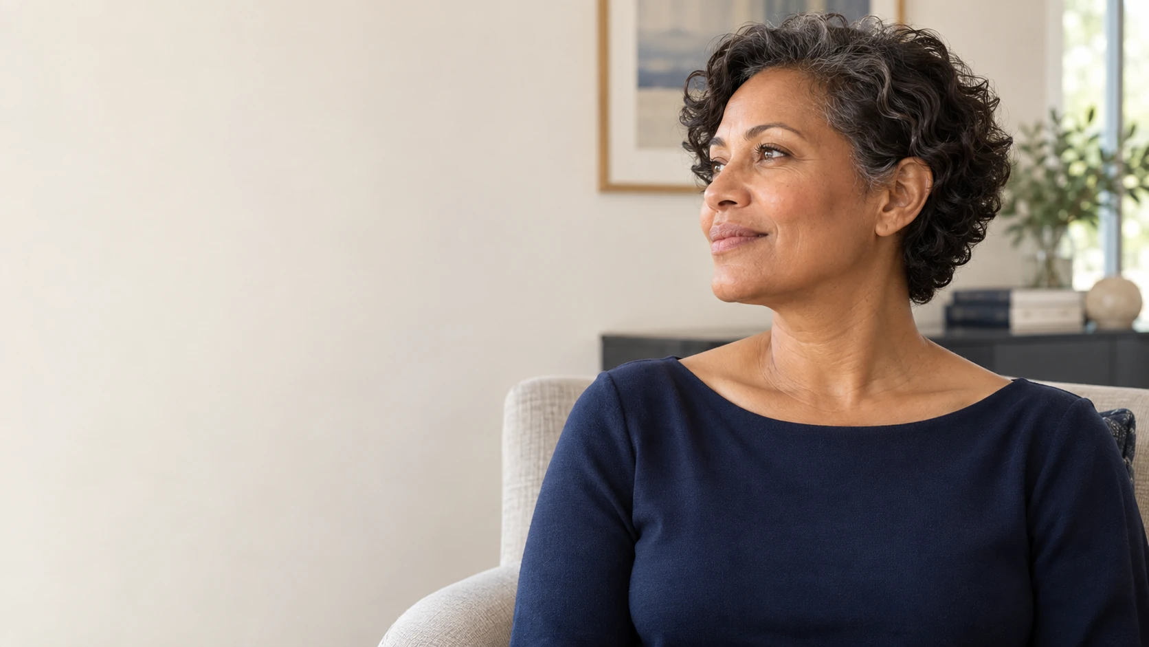 A fictional adult woman sits in a calm room, with her natural jawline and neck visible in a relaxed three-quarter profile.