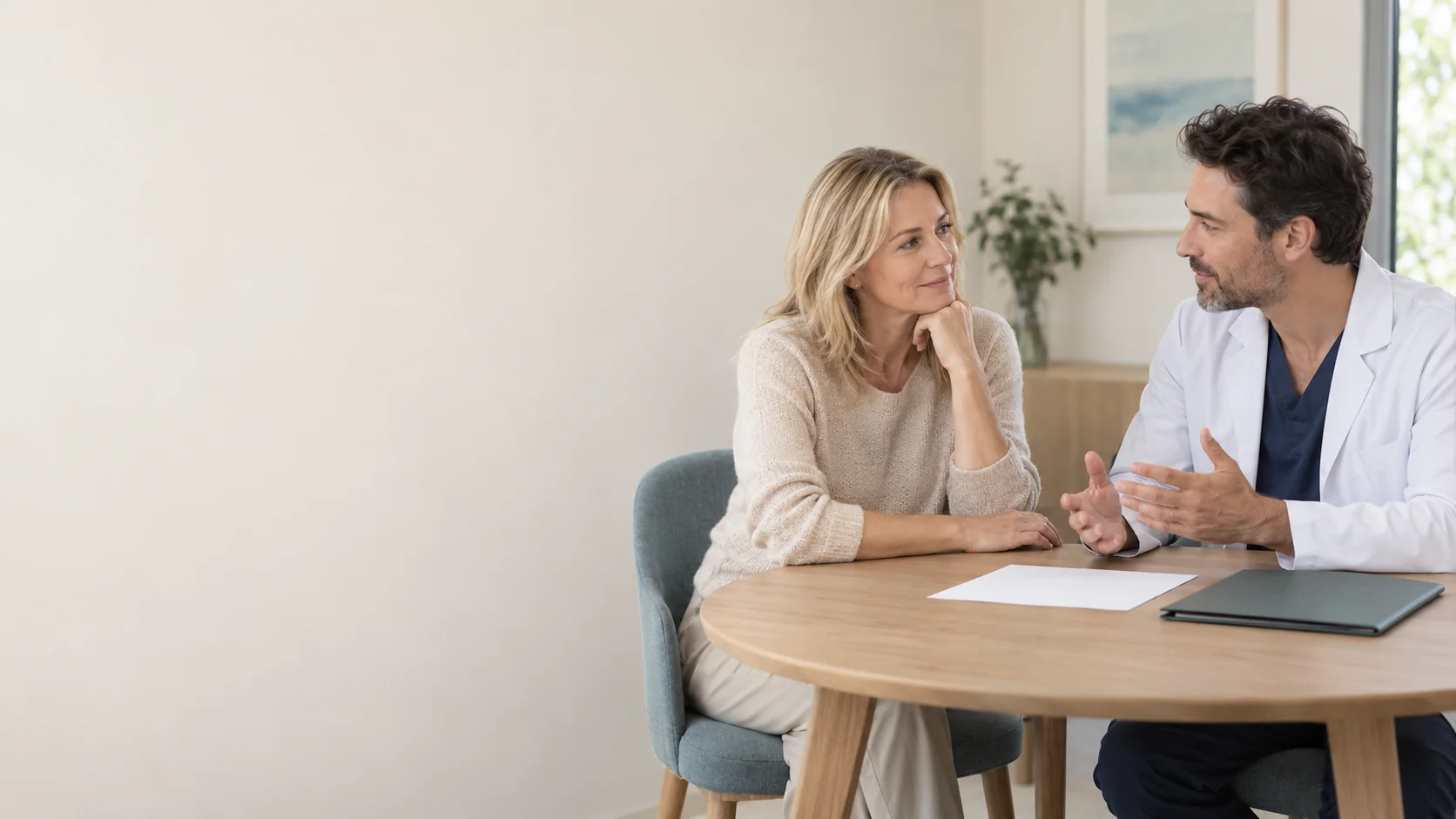 Two adults talking across a table with a blank sheet of paper; one wears a white coat.