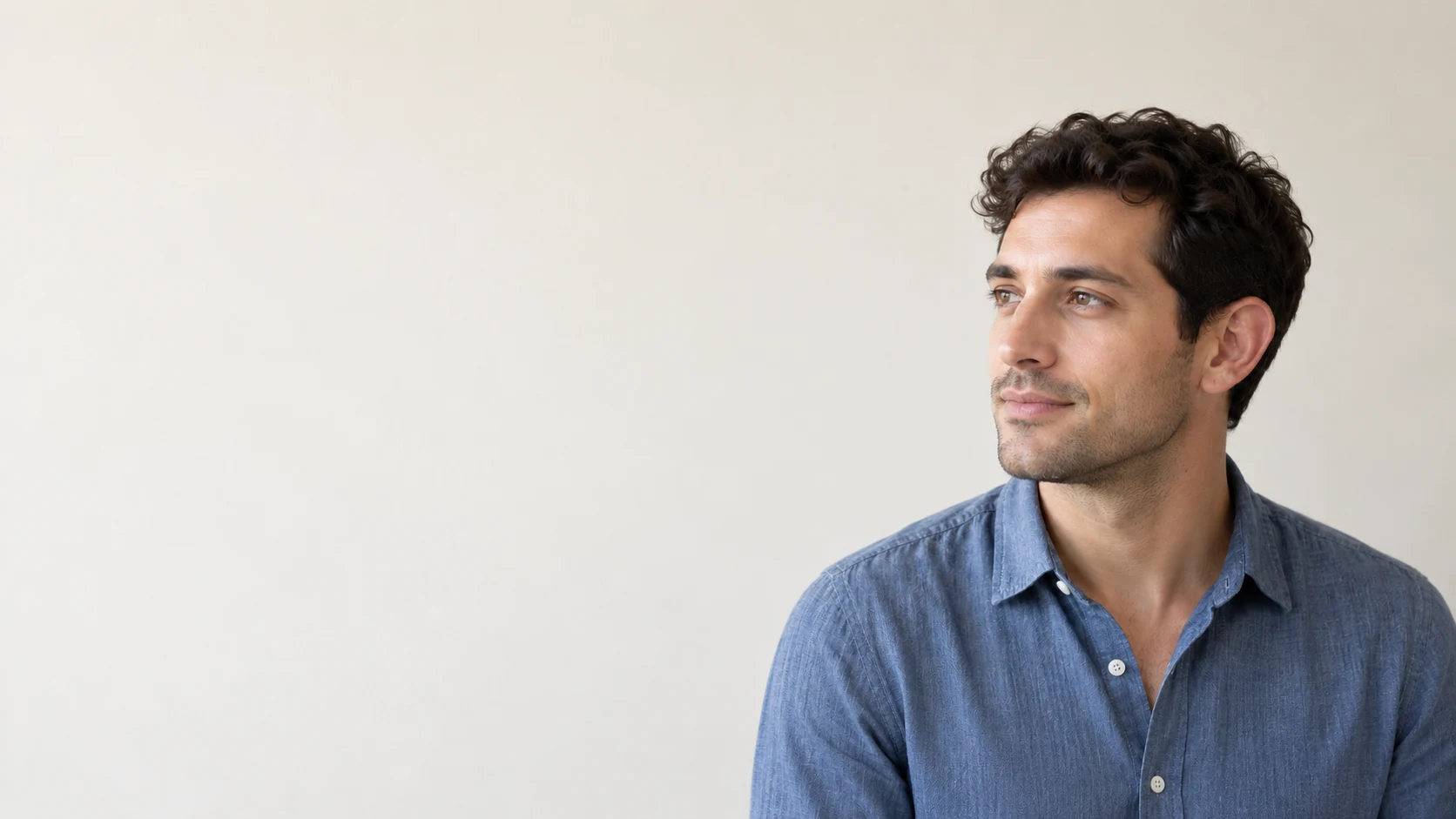 A fictional adult man in a blue shirt with one naturally visible ear against a pale wall.